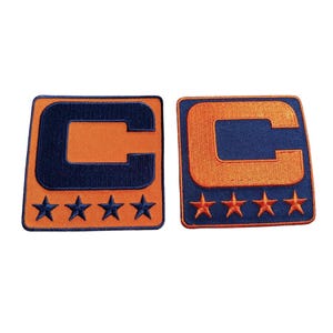 May include: Two embroidered patches with a navy blue "C" on an orange background. Each patch has four orange stars at the bottom. The patches are square with rounded corners.