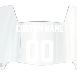 May include: Clear plastic football helmet facemask with a white custom name and number "00" printed on it.