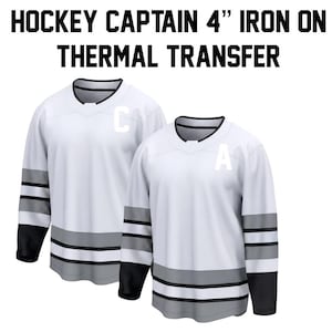 May include: Two white hockey jerseys with black and grey accents. The jerseys have the letters "C" and "A" on the front. The text "HOCKEY CAPTAIN 4" IRON ON THERMAL TRANSFER" is at the top.