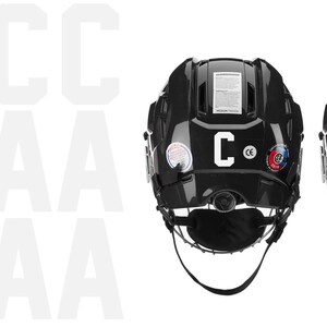 May include: Two black hockey helmets, viewed from the back, are displayed against a white background. One helmet has a white "C" and the other has a white "A". Both helmets have a chin strap and various stickers.