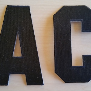 May include: Two black felt letters, A and C, with a slightly distressed look. The letters are uppercase and have a simple, blocky font.