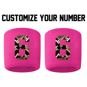 Peut inclure: Deux bracelets de poignet roses avec un numéro 6 imprimé en motif peau de serpent. Le texte "CUSTOMIZE YOUR NUMBER" est au-dessus des bracelets.