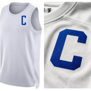 May include: White athletic tank top with a blue "C" on the chest. The tank top has a round neckline and a mesh-like texture. The close-up shows the blue "C" in detail.