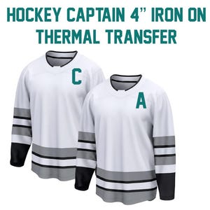 May include: Two white hockey jerseys with black and gray stripes on the sleeves and bottom. One jersey has a teal "C" and the other has a teal "A". Text at the top reads "HOCKEY CAPTAIN 4" IRON ON THERMAL TRANSFER."