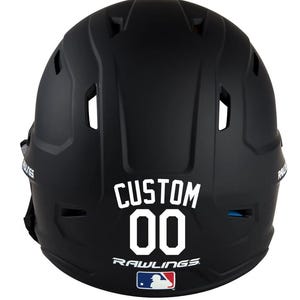 May include: A black baseball helmet with the word "CUSTOM" and the number "00" in white lettering. The Rawlings logo and MLB logo are also visible. The helmet is designed for protection during baseball games.