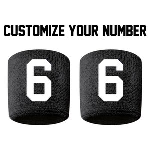 May include: Two black wristbands with the number 6 in white. The text "CUSTOMIZE YOUR NUMBER" is above the wristbands in bold, black letters. The wristbands are made of a textured material.