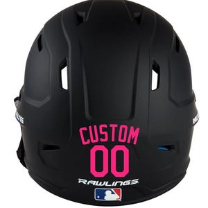 May include: Black baseball helmet with the word "CUSTOM" and the number "00" in pink. The Rawlings logo and MLB logo are below the number. The helmet has several vents and is designed for protection.