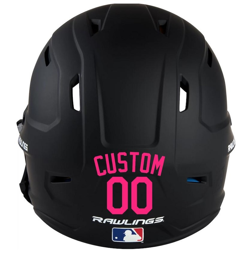 May include: Black baseball helmet with the word "CUSTOM" and the number "00" in pink. The Rawlings logo and MLB logo are below the number. The helmet has several vents and is designed for protection.