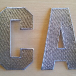 May include: Two grey felt letters, C and A, with white stitching around the edges.