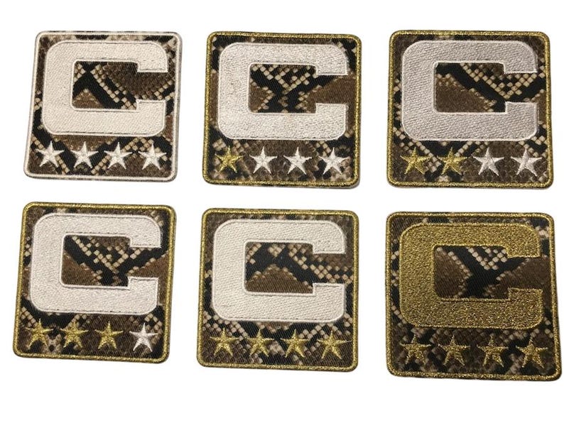 Puede incluir: Seis parches bordados con la letra may&uacute;scula "C" en blanco, plateado y dorado. Cada parche tiene un fondo con estampado de piel de serpiente y una fila de cinco estrellas.