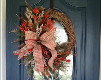 May include: A fall-themed wreath with a red and white plaid bow, brown twigs, and red and orange leaves. The wreath is hanging on a blue door with a glass window.