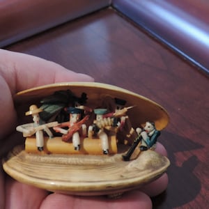 Könnte beinhalten: Eine kleine Gruppe von geschnitzten Holzfiguren sind in einer Muschel angeordnet. Die Figuren sind in bunten Kleidern gekleidet und spielen Musikinstrumente. Die Muschel ist geöffnet und die Figuren sind im Inneren sichtbar.