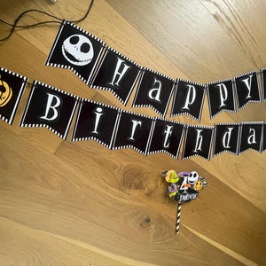 Op de afbeelding: Zwart-wit banner met de tekst "Happy Birthday" en Jack Skellington en pompoen ontwerpen. Een taarttopper met Jack Skellington en andere personages is ook aanwezig.