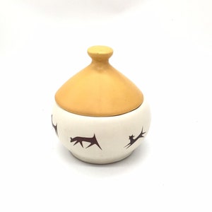 May include: A small, round, white ceramic jar with a yellow lid. The jar has a stylised design of black animals on the sides.