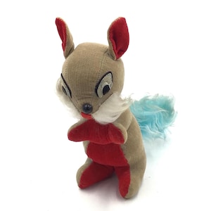 May include: A vintage plush squirrel toy with a tan body, red accents on the ears, paws, and chest, and a blue fluffy tail. The squirrel has black and white eyes, a white beard, and a red tongue.