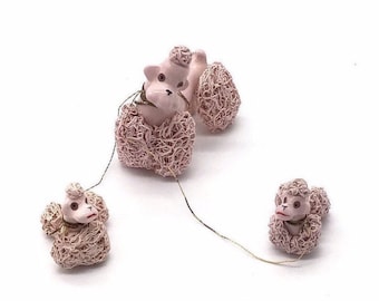 May include: Three pink ceramic poodle figurines with curly hair. The poodles are connected by a string, suggesting a playful scene.