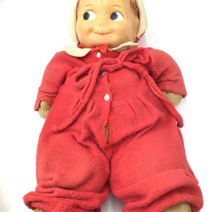 May include: A vintage plush doll with a red and white outfit. The doll has a smiling face with blue eyes and brown hair.