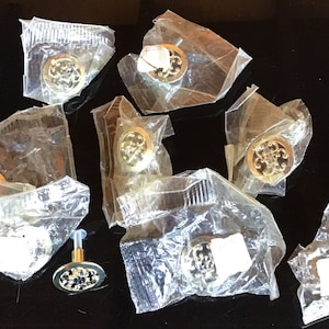 May include: Eight gold cabinet knobs with intricate designs are packaged individually in clear plastic bags. The knobs are ready to be used for home decor projects.