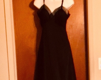 May include: A black sleeveless dress with a lace trim neckline hanging on a hanger against a brown wooden door.