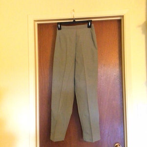 May include: A pair of khaki-colored pants hanging on a hanger against a wooden door. The pants have a straight leg and a high waist.