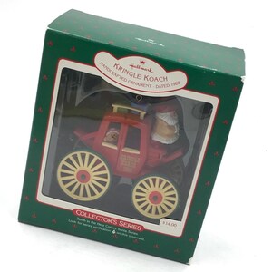 May include: A Hallmark Kringle Koach handcrafted ornament from 1988, featuring a red carriage with yellow wheels and a Santa figure, enclosed in a green box with red accents. The box displays the text Kringle Koach Handcrafted Ornament Dated 1988.