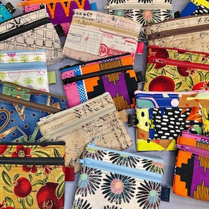 May include: A collection of small, colorful zippered pouches with various patterns. Designs include floral, geometric, and vintage-inspired prints. Each pouch has a different color zipper and a small fabric tag.