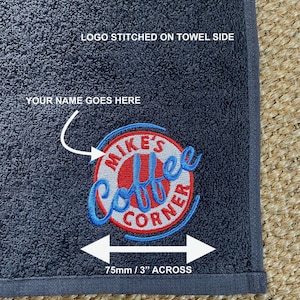 May include: A dark gray towel with a red, white, and blue embroidered logo that says "Mike's Coffee Corner". The logo is 3 inches across. The text "LOGO STITCHED ON TOWEL SIDE" and "YOUR NAME GOES HERE" are printed on the towel.