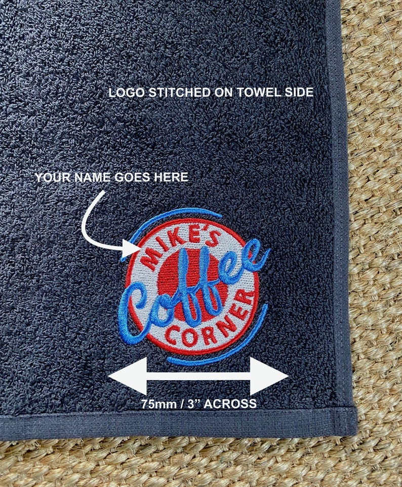 May include: A dark gray towel with a red, white, and blue embroidered logo that says "Mike's Coffee Corner". The logo is 3 inches across. The text "LOGO STITCHED ON TOWEL SIDE" and "YOUR NAME GOES HERE" are printed on the towel.