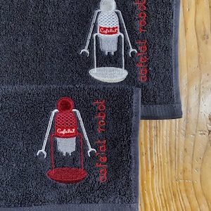 May include: Two dark gray hand towels with embroidered images of a robot holding a coffee maker. The text "Cafelat Robot" is embroidered on each towel.