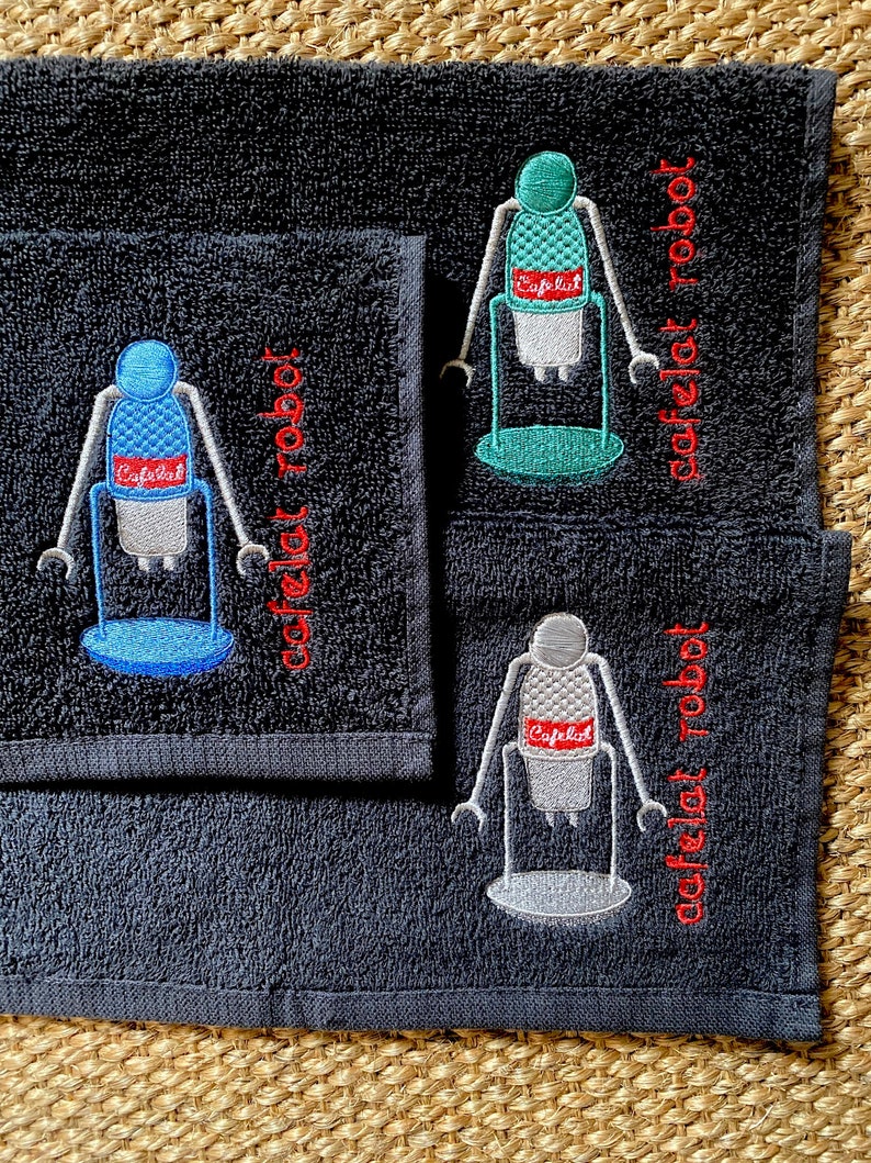 May include: Three black hand towels with embroidered images of a robot holding a coffee cup. The text "cafelet robot" is embroidered in red on each towel.