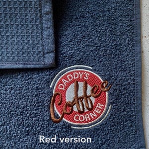 May include: A dark blue kitchen towel with a red and white embroidered logo that says "Daddy's Coffee Corner".
