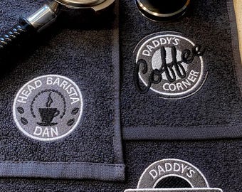May include: Two black cotton towels with embroidered logos. The top towel has a logo that says "Daddy's Coffee Corner" and the bottom towel has a logo that says "Daddy's Coffee Station".
