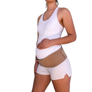 May include: A pregnant person wearing a white tank top and white shorts with a beige pregnancy support belt.