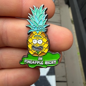 May include: A metal enamel pin shaped like a yellow pineapple with a cartoon face, green leaves, and a green puddle base. The text on the base reads IM PINEAPPLE RICK!! The design features black outlines and vibrant yellow, green, and white colours.