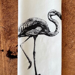 May include: A white linen tea towel with a black and white illustration of a flamingo. The text "Ivory linen" is printed at the top of the towel.