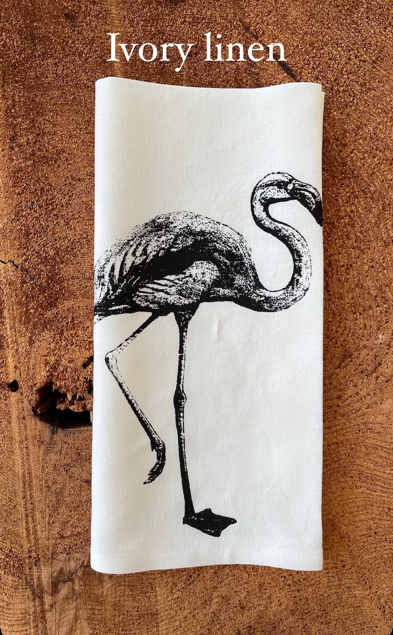 May include: A white linen tea towel with a black and white illustration of a flamingo. The text "Ivory linen" is printed at the top of the towel.