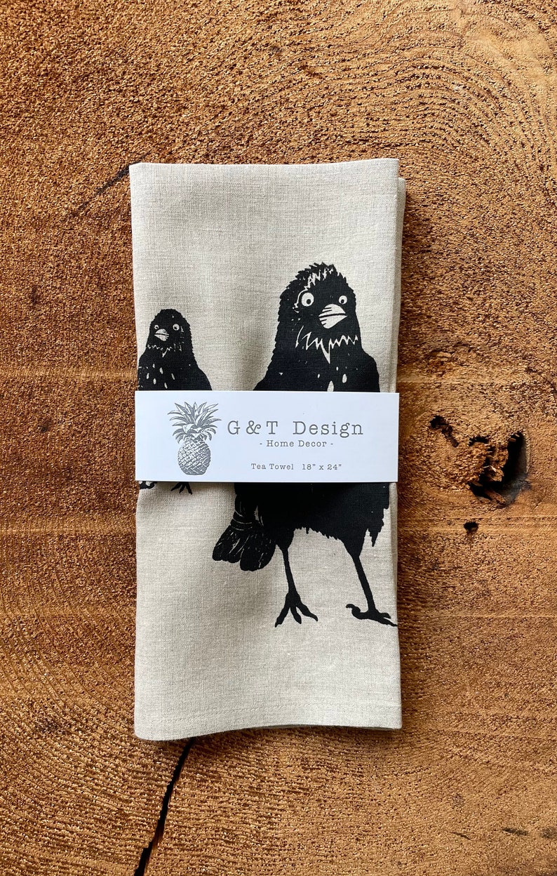 May include: A linen tea towel with a black and white illustration of two birds. The towel is 18 inches by 24 inches and has a label that reads "G&T Design - Home Decor - Tea Towel 18" x 24".