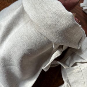 Pode incluir: Uma bolsa de linho branca com fecho de cord&atilde;o. A bolsa est&aacute; dobrada e o cord&atilde;o est&aacute; amarrado. A bolsa est&aacute; vazia.