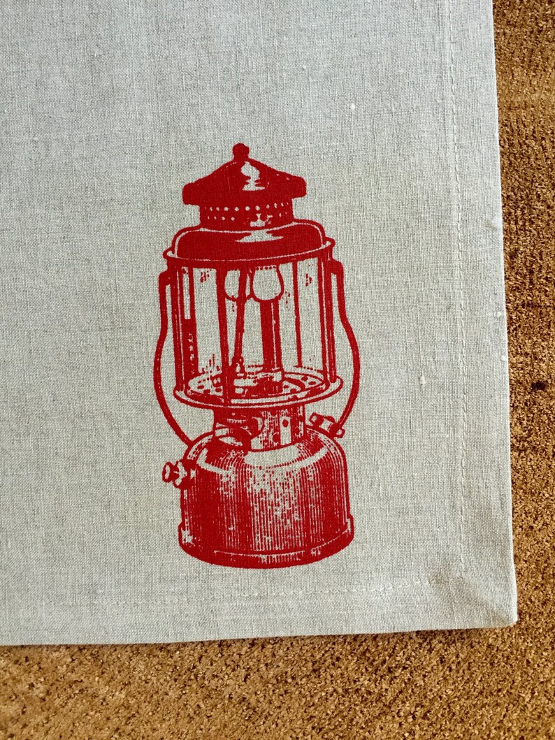 May include: Red vintage lantern printed on a white linen tea towel. The lantern has a round glass globe and a metal handle.