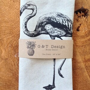 May include: A black and white illustration of a flamingo on a white tea towel. The towel is labeled "G&T Design - Home Decor - Tea Towel 18" x 24"