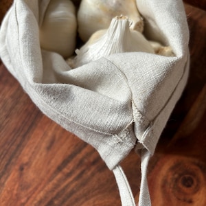 Pode incluir: Uma bolsa de linho branca para produtos com fecho de cord&atilde;o, cheia de bulbos de alho.