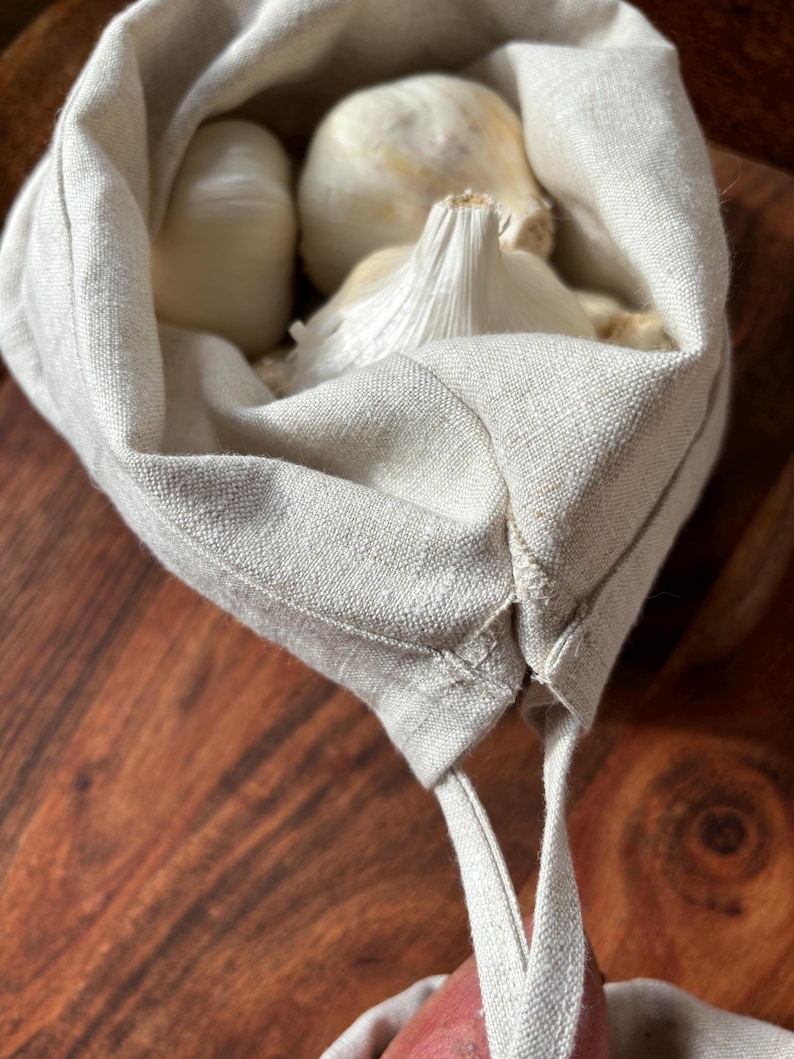 Pode incluir: Uma bolsa de linho branca para produtos com fecho de cord&atilde;o, cheia de bulbos de alho.