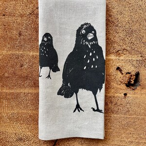 May include: A linen tea towel with a black and white print of two birds. The birds are stylized and have a simple design.