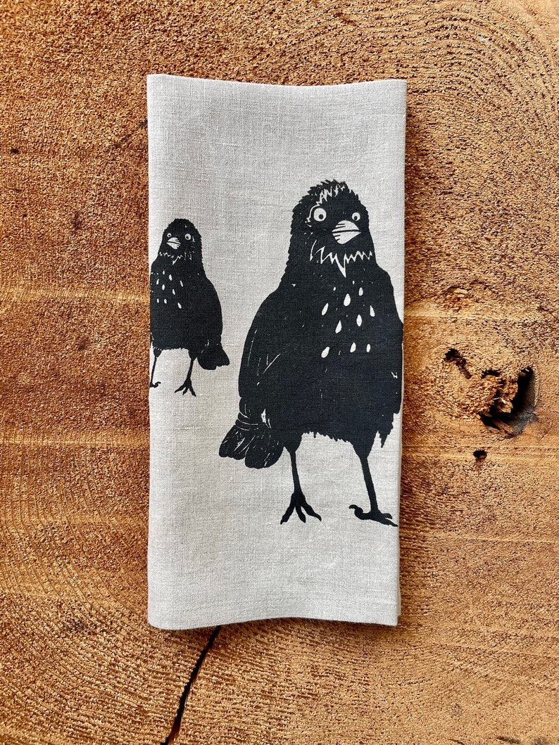 May include: A linen tea towel with a black and white print of two birds. The birds are stylized and have a simple design.