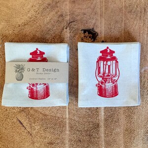 May include: Two white cotton cocktail napkins with a red vintage lantern design. The napkins are stacked and feature the text "G&T Design - Home Decor - Cocktail Napkin 12" x 12"