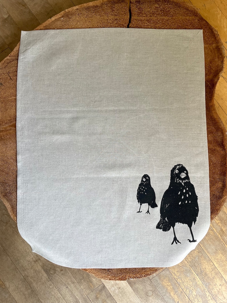 May include: A white linen tea towel with a black silhouette of two birds printed on it.