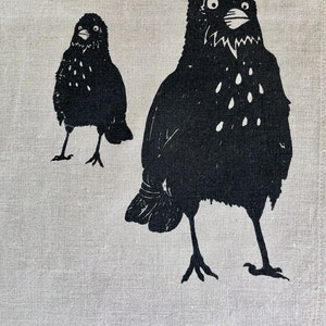 May include: Two black birds with white spots are depicted on a white linen background. The larger bird is facing forward with its beak open, while the smaller bird is facing to the left.