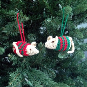 May include: Two crocheted mouse ornaments hanging on a Christmas tree. The mice are wearing red and green striped sweaters.