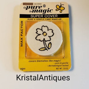 May include: A vintage compact of Pure Magic Super Cover cake makeup in Sun Bronze. The compact features a yellow flower design on a white background. The text on the packaging reads "Pure Magic Super Cover Pure & Gentle Cake Make-Up" and "covers blemishes like magic! - pure & gentle - dermatologist tested".