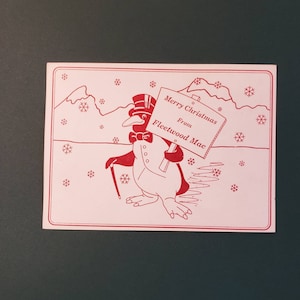 May include: A red and white Christmas card featuring a penguin wearing a top hat and bow tie, holding a sign that reads "Merry Christmas from Fleetwood Mac".